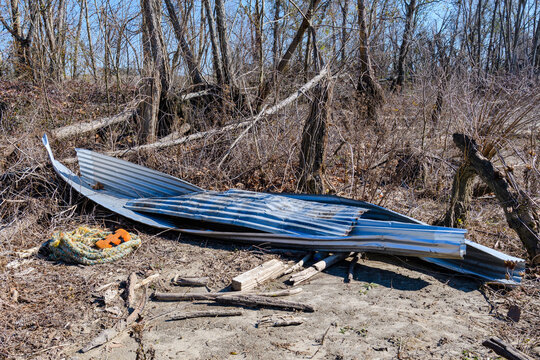 Bent windblown sheet metal on the bank of the Mississippi River next to trees broken by Hurricane Ida