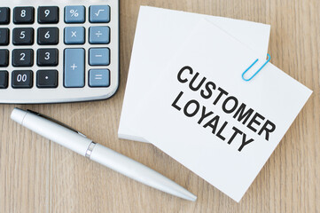 CUSTOMER LOYALTY text on a white card on a paper clip on a wooden table next to a pen and calculator