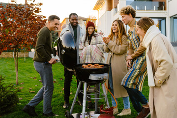 White man grilling meat during barbeque with his friends on backyard