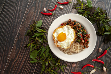Pad Kra Pao Moo Sab with Kai Dao on wooden backgound, Thai famous food, the stir-fried minced pork, garlic, basil and chili topped with fried egg. This is hot and spicy. Used in menu for restaurant.