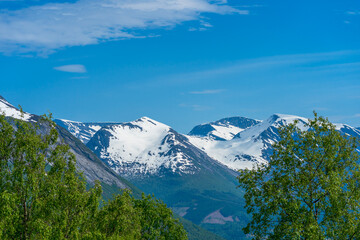 Spring time in Norway with mountains with snow and green trees.