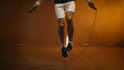 Cropped view of athletic sportsman jumping with rope on dark background - obrazy, fototapety, plakaty