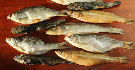 Sea salted smoked fish on a brown red wooden background. Smoked smelt, pike perch, goby, ram....