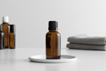Amber glass essential oil bottle mockup with towel on the white table.
