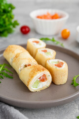 Thin pancake rolls or crepes rolls with smoked salmon, cream cheese, cucumber and dill on a gray concrete background. Selective focus.