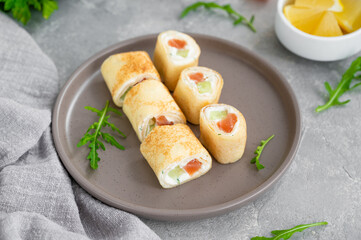 Thin pancake rolls or crepes rolls with smoked salmon, cream cheese, cucumber and dill on a gray concrete background. Selective focus.