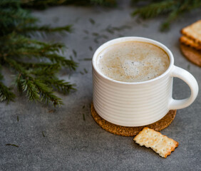 white ceramic mug of coffee with milk on a background of green spruce branches