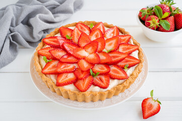 Strawberry tart with custard cream on a plate on a white wooden background. Copy space.