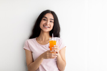 Cheerful young Indian woman holding glass of fresh orange or mango juice on white background, copy space