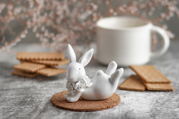 A white ceramic mug with milk, biscuits and a white ceramic bunny surrounded by small white flowers. A gentle breakfast in a light key