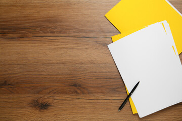 Yellow files with blank sheets of paper and pen on wooden table, flat lay. Space for text