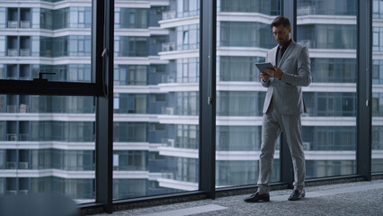 Focused entrepreneur using tablet researching corporate data in office building.