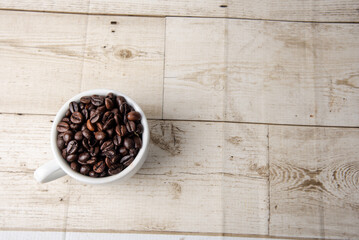 Arabica and Robusta roasted coffee beans in white glass on wooden background cutout