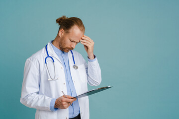 Puzzled male doctor wearing lab coat posing with clipboard