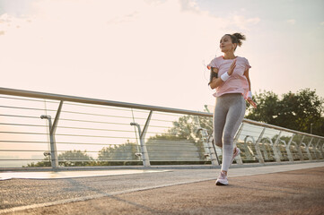Young athletic woman, jogger, runner practicing sport outdoors, running fast along the bridge over...