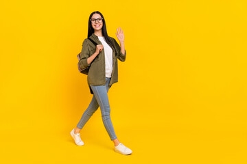 Full body photo of impressed millennial lady go wave wear bag spectacles shirt jeans footwear isolated on yellow background
