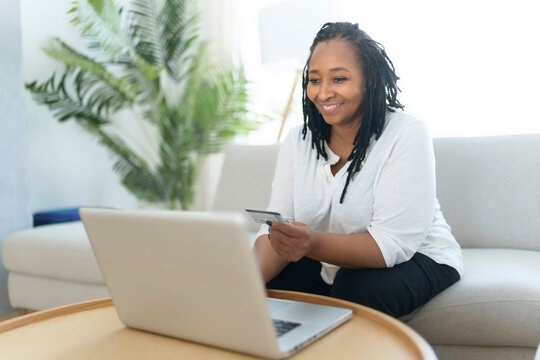 Photo of pretty black woman using laptop at home sofa and buy something on the web