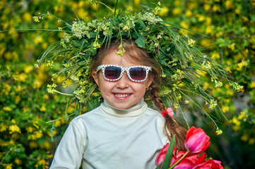Portrait of a cheerful little girl in sunglasses and a wreath of field herbs
