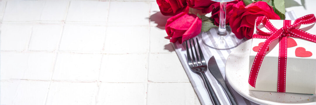  Valentine Day Table Setting With Plate, Gift Box With Festive Red Ribbon, Wine Glass, Fork And Knife, Red Roses Flowers Bouquet White Tiled Table Flatlay Copy Space