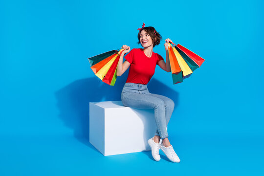 Full body photo of young cheerful lady look empty space hold shooping bags isolated over blue color background