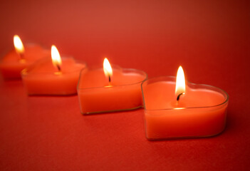 Fototapeta na wymiar Four red burning heart-shaped candles with blazing flames. Tongues of fire on a red background. Valentine's Day, passion, love, feelings concept. Monochrome wallpaper. I love you decor for February 14