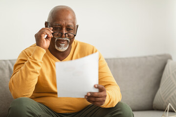 Contented Senior Black Man Reading Papers Wearing Eyeglasses At Home - Powered by Adobe