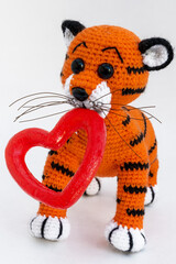 Handmade amigurumi doll tiger cub is standing next to a red heart..The background is white. isolate.