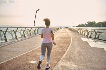 Back view of young athletic woman, jogger, runner practicing sport outdoors, running fast along the...