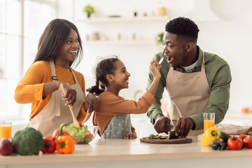 Black Family Cooking, Daughter Feeding Father While Making Salad Indoor