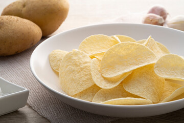 Close up crispy potato chips snack in white plate on wooden table
