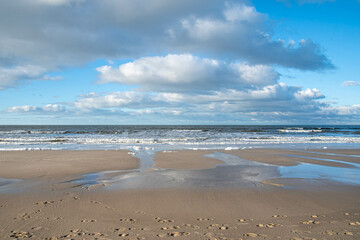 Weißer Schaum am Strand und Wolken spiegeln sich im Wasser 