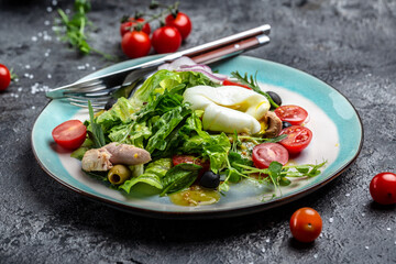 Tuna salad with poached, egg, lettuce, cherry, tomatoes olives and corn on dark stone or concrete background. Top view. copy space