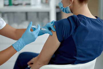 woman doctor holding syringe making covid 19 vaccination injection dose in shoulder of female patient. Flu influenza vaccine clinical trials concept, corona virus treatment side effect, inoculation