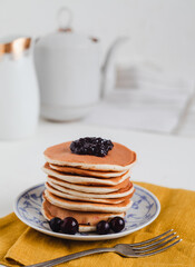 Homemade classic american pancakes with black currant jam on a yellow napkin on a light background. Sweet pancakes with berries.