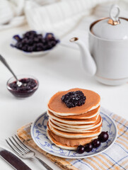 Breakfast with homamade pancakes with jam, berries and kettle on a light background.