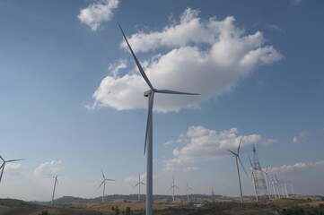 Evening atmosphere of Windmills farm field with white clouds scattered against the blue sky. The electricity energy generating wind turbine. The concept of using the use of renewable wind to generate 