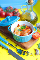 Baked shrimps with tomatoes, garlic, lemon, olive oil and mint in blue bowls on a yellow background