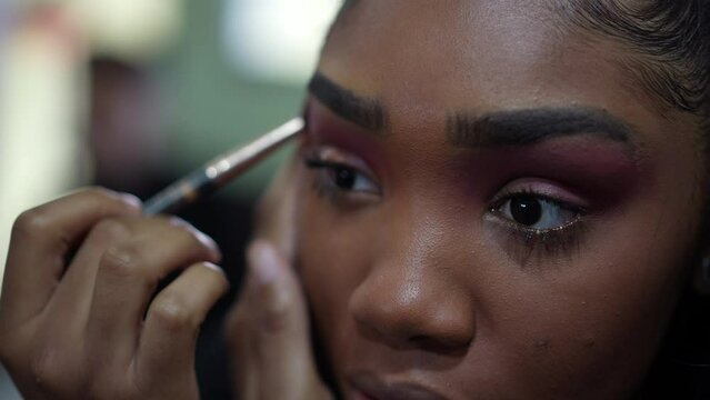 A young black girl applying make-up in front of mirror