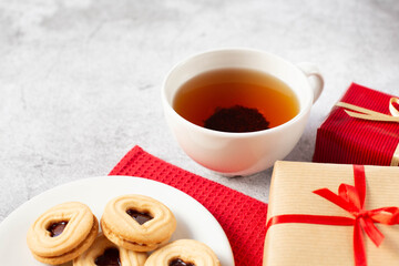A white cup of tea, packaged gifts and a plate of cookies are on the table. Theme breakfast for Valentine's Day. Free space for text.