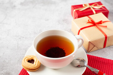 A white cup of tea with one cookie, packaged gifts are on the table. Theme breakfast for Valentine's Day. Free space for text.