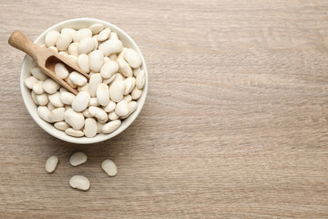 Raw white beans, bowl and scoop on wooden table, flat lay. Space for text