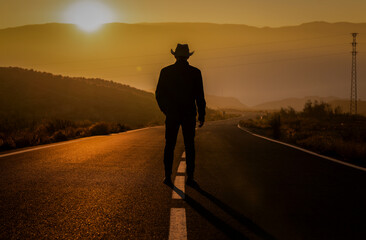 Silhouette of adult man in cowboy hat standing on country road during sunset. Almeria, Spain