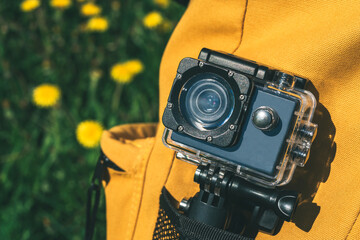 Close-up, yellow backpack with an action camera in the pocket. Against the backdrop of nature fields with dandelions.