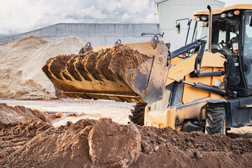The excavator loader works with a bucket for transporting sand at a construction site. Professional...