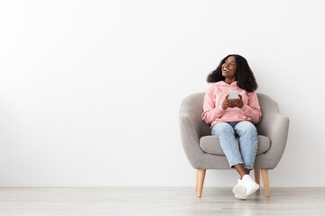 Joyful black lady sitting at arm chair with mobile phone