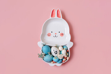 Cute plate in the shape of a bunny with  Easter eggs and candy on pink background. Happy Easter concept.