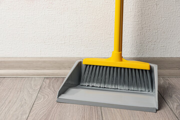 Plastic broom with dustpan on wooden floor indoors