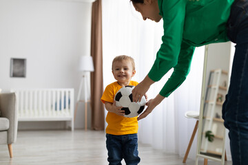Happy caucasian mother and her toddler son playing with soccer ball at home, having fun and...