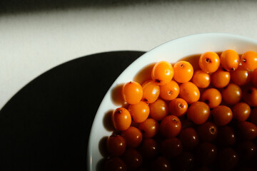 Organic sea buckthorn in a white plate. Layout on a gray table, flat lay. Fresh orange berries in bright sunlight. Natural valuable food supplement.