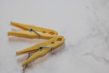 Two yellow classic plastic clothespins with copy space to the right from a surface with marble structure